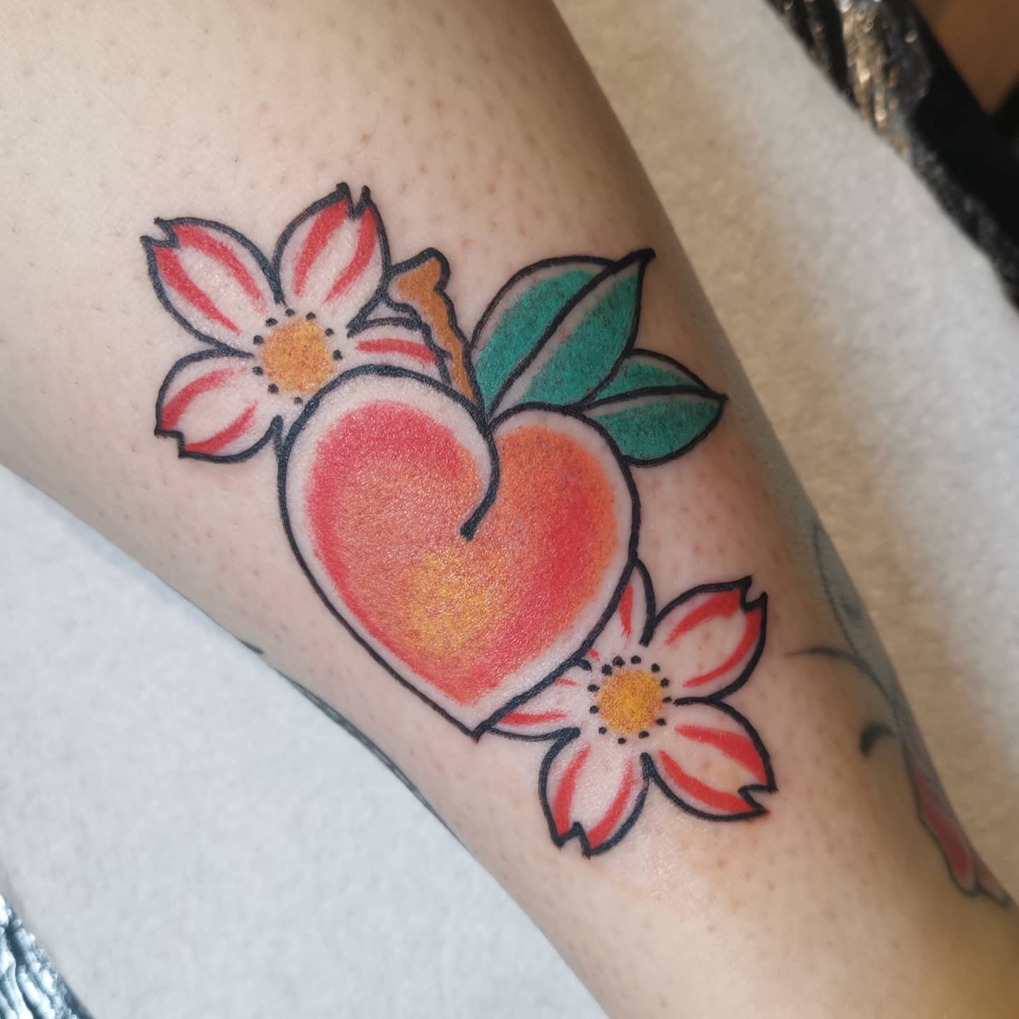 Tattoo of a heart-shaped peach with two flowers and green leaves on skin